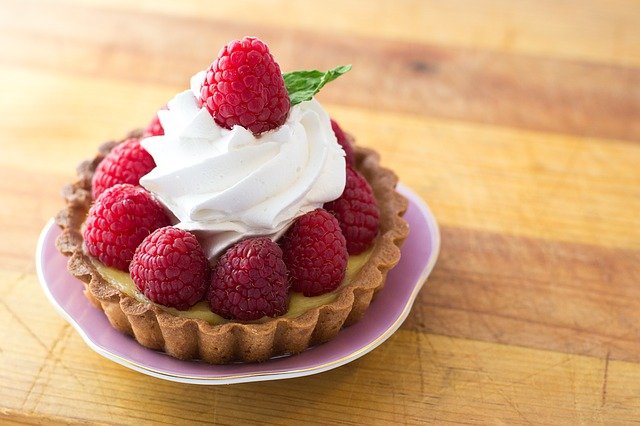 Raspberry tart with whipped cream in a dish on a wooden table