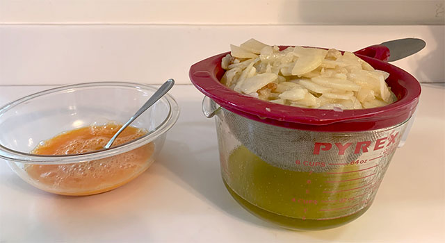 Beaten eggs in a bowl on a countertop beside a colander of sliced potatoes and onions draining into a one-quart Pyrex measure