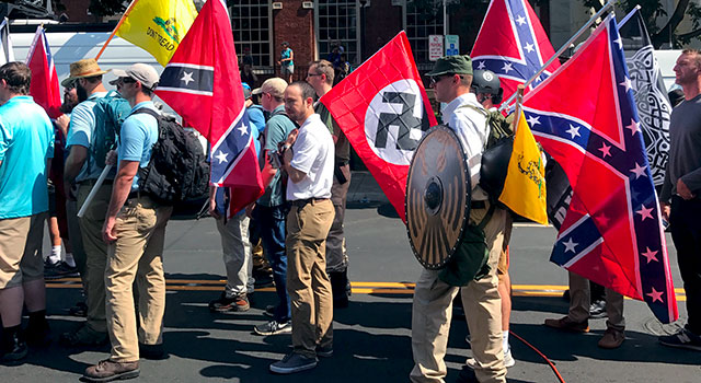 Men lined up in the street, holding Gadsden flags, Nazi flags, and rebel flags